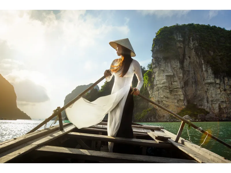 Mujer vietnamita con sombrero cónico en un paseo en barco por la Bahía de Halong al atardecer