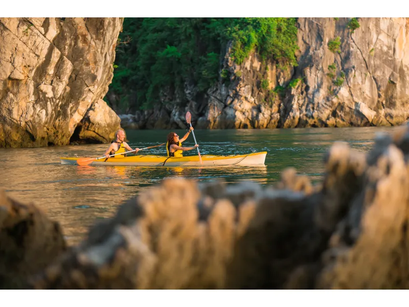 Pareja remando en kayak al atardecer en la Bahía de Halong entre acantilados