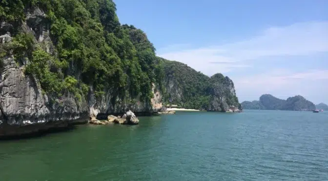 Paisaje costero de la bahía de Lan Ha con acantilados verdes y aguas cristalinas, ideal para turismo sostenible en Vietnam