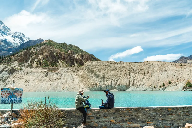 Excursionistas descansando junto al lago Gangapurna en un viaje cultural y de naturaleza en Nepal.