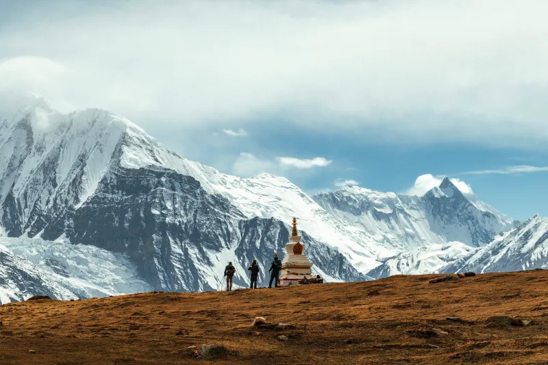 Grupo de montañeros frente a estupa budista con fondo de picos nevados en Annapurna, Nepal.