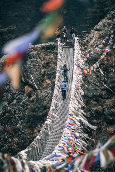 Puente colgante decorado con banderas de oración en trekking del Himalaya, Nepal.