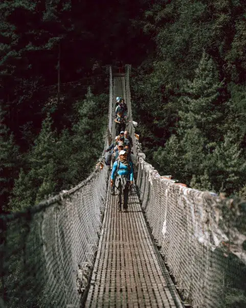 Grupo de excursionistas cruzando puente colgante en ruta al Everest, Nepal.