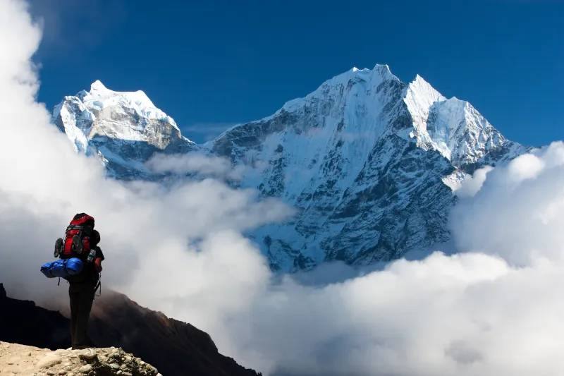Excursionista con mochila frente a montañas nevadas cubiertas de nubes en Nepal.